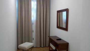 A room with a wooden floor, a small white bench, a wooden desk, and a mirror on the wall.