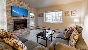 Una sala de estar con chimenea de piedra, un televisor de pantalla plana, una mesa de centro de vidrio y un sofá con cojines estampados.