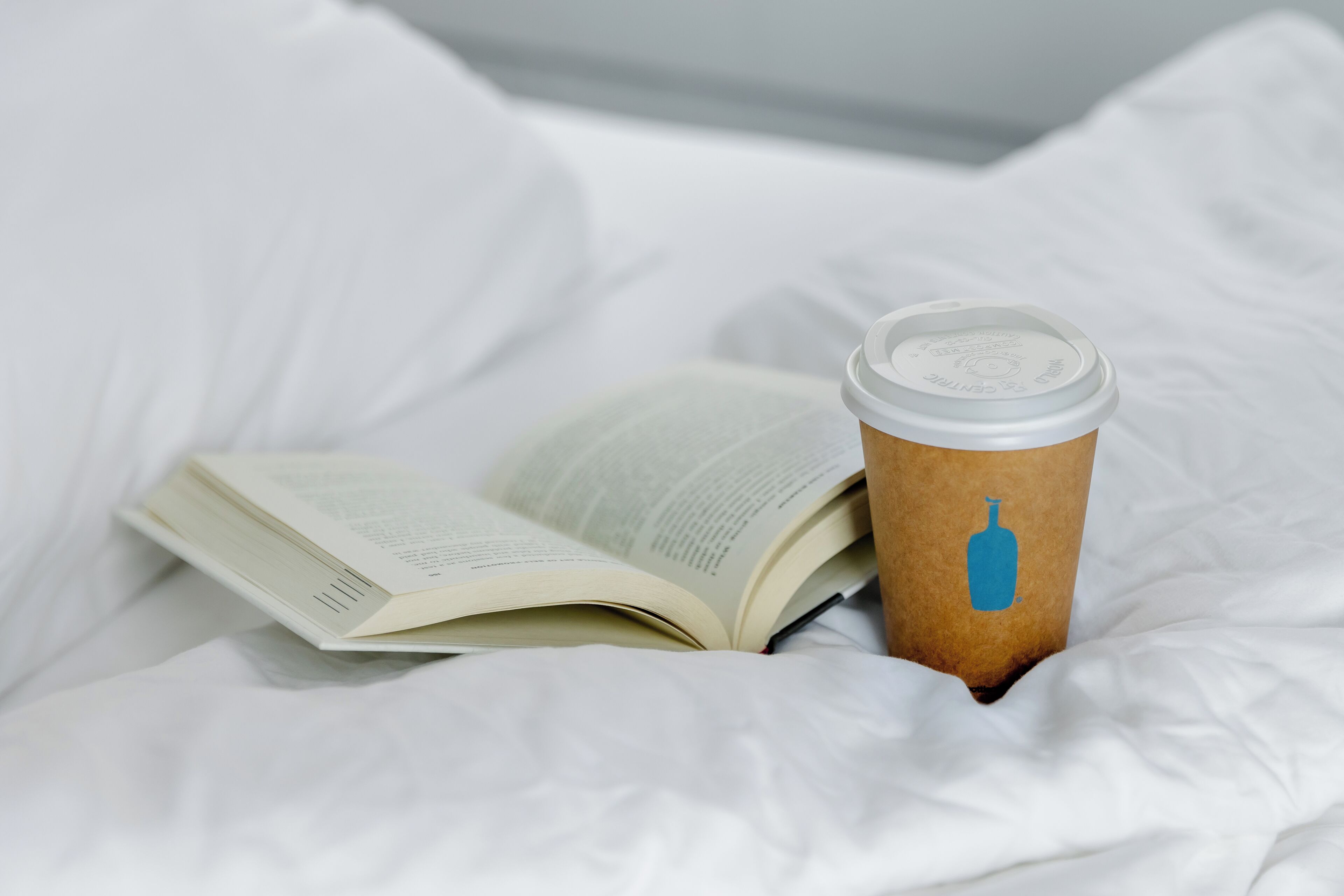 A book and a coffee cup on a bed.