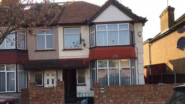 A two-story house with a red front door, a small front porch, and a brick wall. - Le Buffle Noir Londres (London)