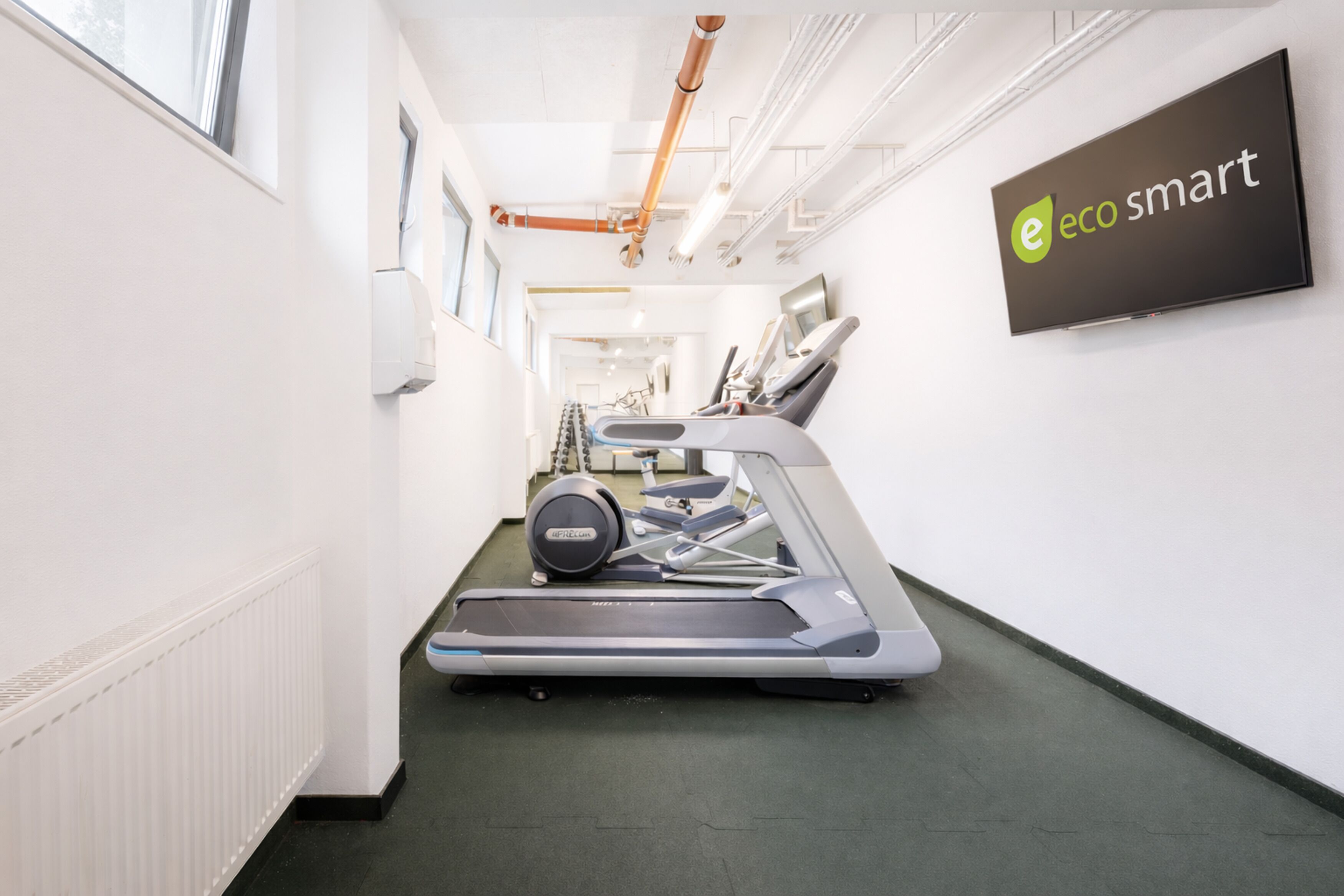 A gym with a treadmill, a wall-mounted TV, and a sign reading "eco smart".