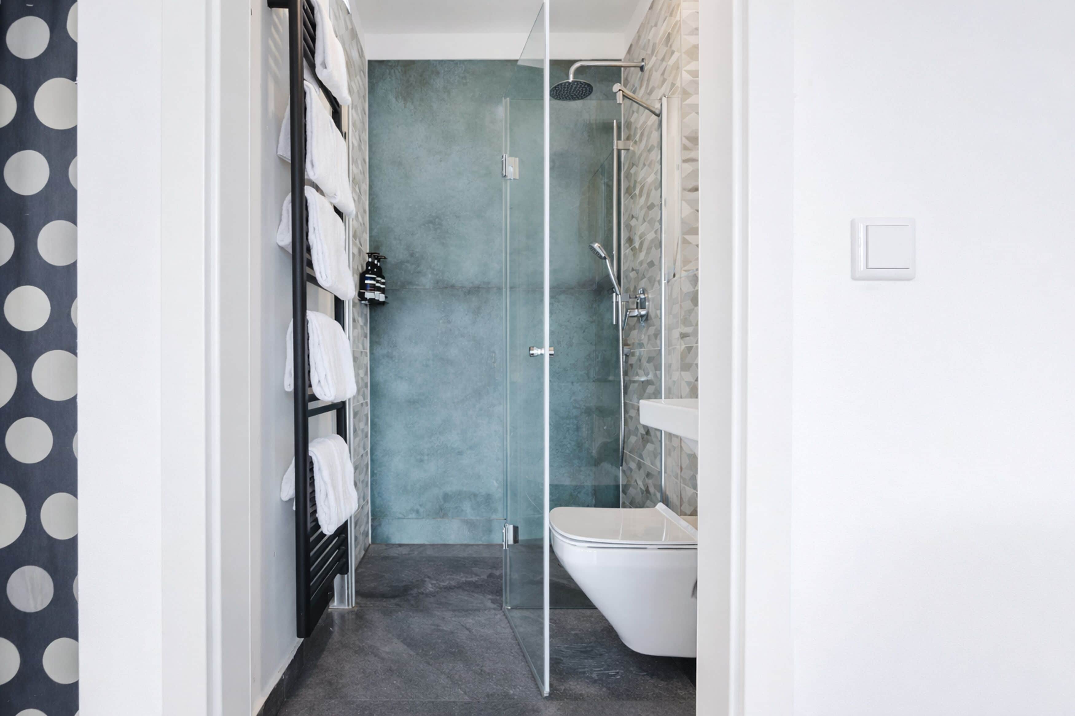 Une salle de bain moderne avec une douche à parois de verre, des toilettes blanches et un porte-serviettes avec des serviettes blanches.