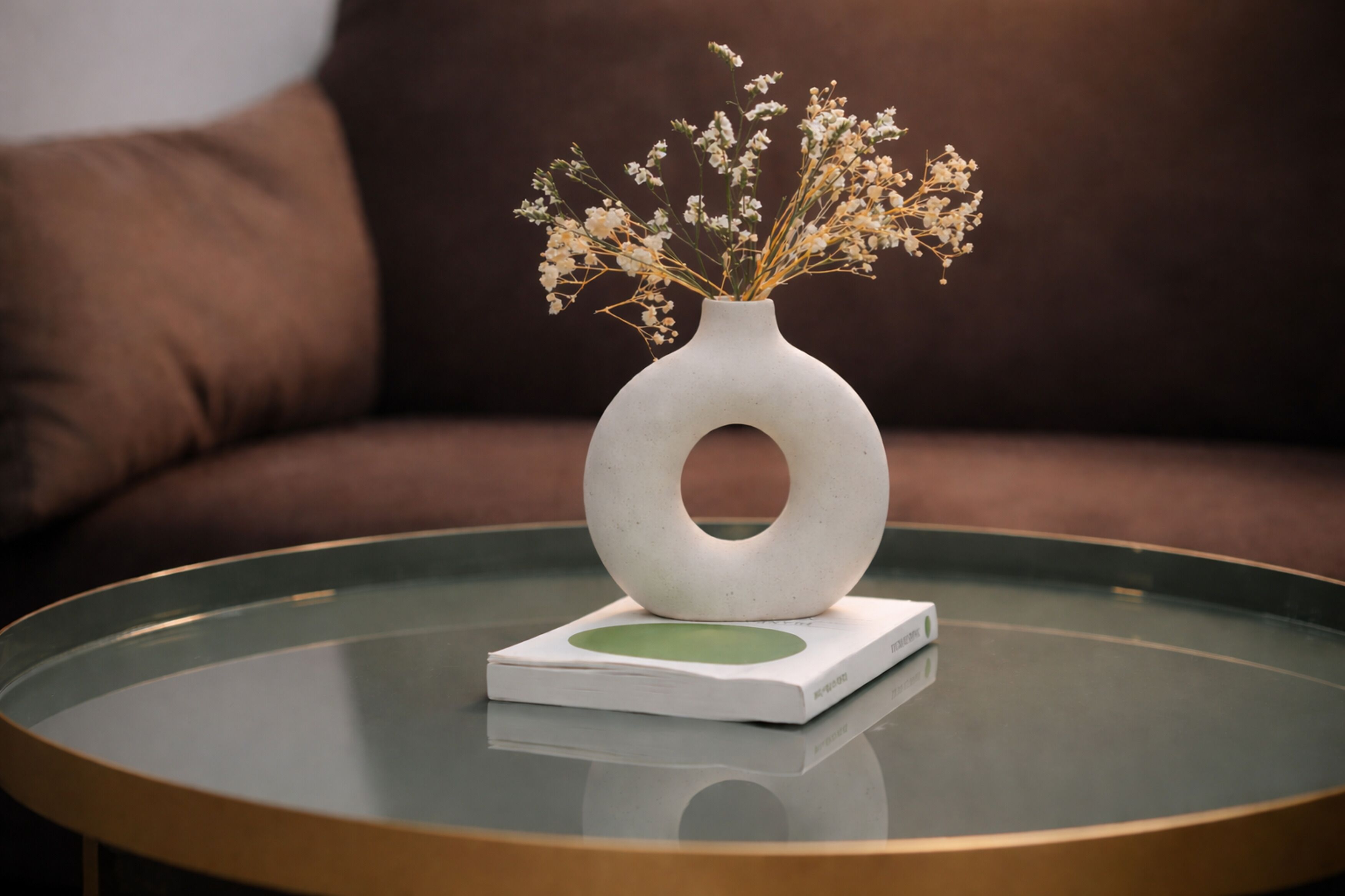 A white vase with a circular cutout on a glass table, placed on a white base with a green circle.