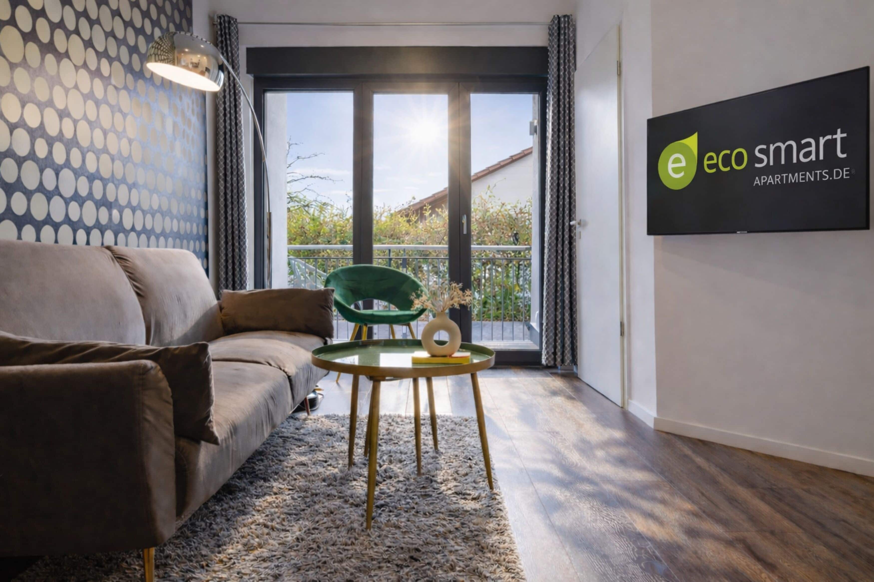 A modern living room with a sofa, a green chair, a small table, and a large window with a view of greenery.
