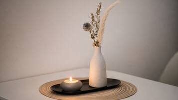 A candle in a white vase on a black tray with a woven mat, placed on a white surface.