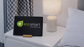A tablet displaying 'eco smart apartments.de' on a bedside table with a lamp and a pillow.