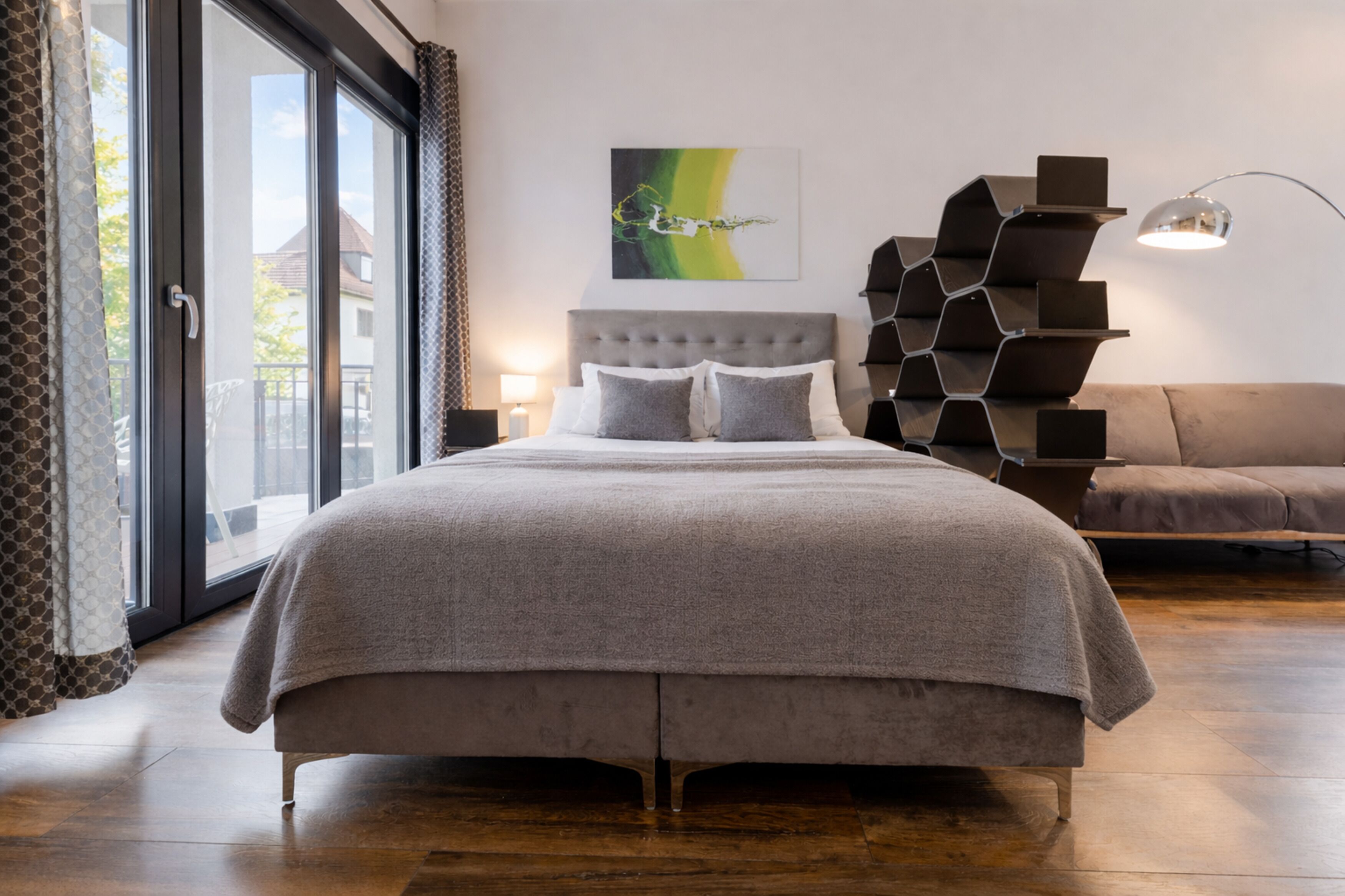 Une chambre à coucher moderne, dotée d’un grand lit, d’une œuvre d’art murale aux motifs géométriques originaux et offrant une vue à travers une porte-fenêtre coulissante.