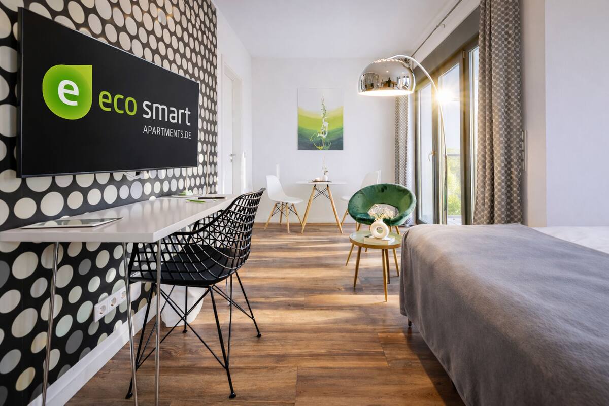 A modern hotel room with a polka dot wallpaper, a bed, a desk with a chair, a small table with a lamp, and a painting on the wall.