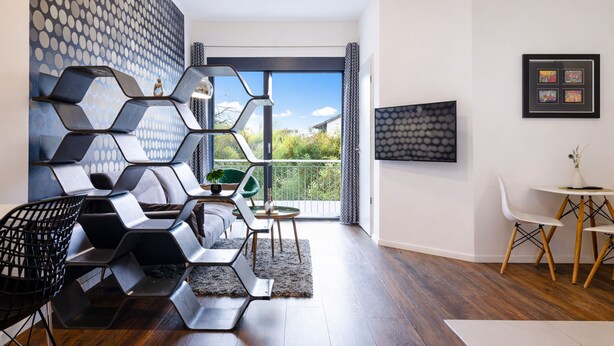 En moderne stue med et geometrisk vægdesign, en grøn lænestol, et rundt bord og et fjernsyn på væggen.