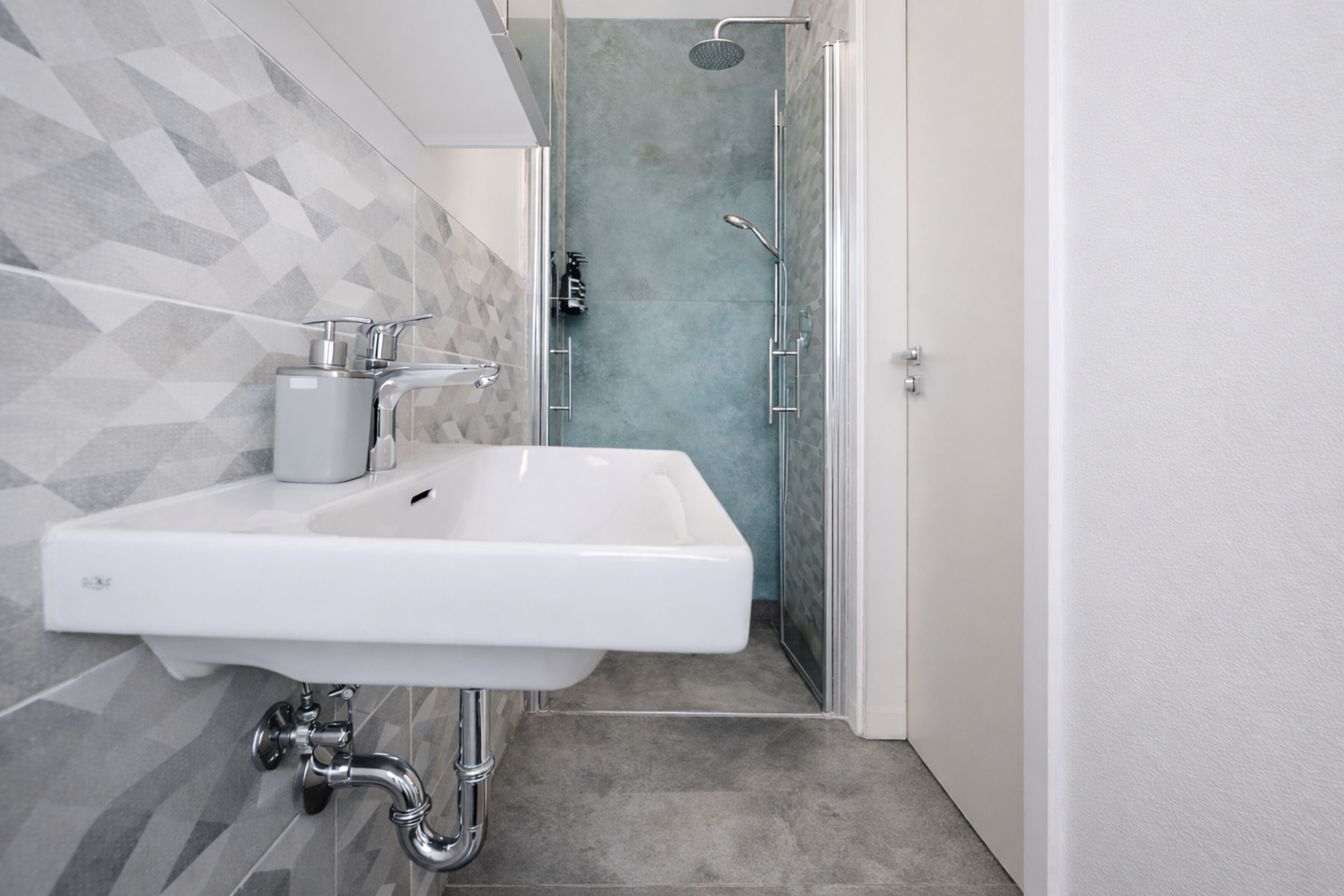 A modern bathroom with a white sink, a shower with a glass door, and a geometric tile backsplash.