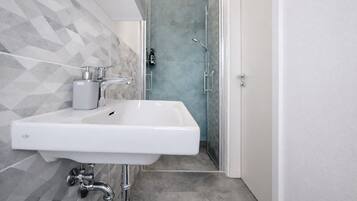 A modern bathroom with a white sink, a shower with a glass door, and a geometric tile backsplash.