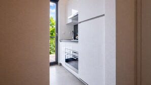 Et moderne køkken med hvide skabe, en indbygget ovn og et vindue med udsigt til en balkon med grønne planter.