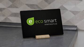 A tablet displaying the logo and name of 'eco smart apartments.de' on a black background with a geometric wall pattern in the background.