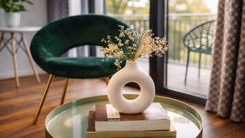 A round glass table with a white vase and books, a green chair, and a balcony view.