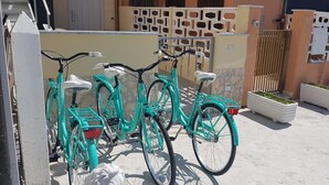A row of turquoise bicycles parked against a wall with a white fence and potted plants nearby.