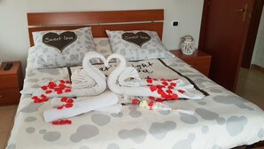 A neatly made bed with heart-shaped pillows, a remote control, and a decorative item on the nightstand.