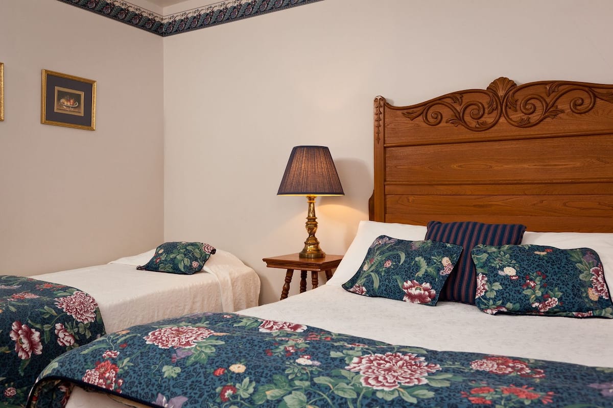 A room with two single beds, each with floral-patterned bedding, a wooden headboard, and a bedside table with a lamp.