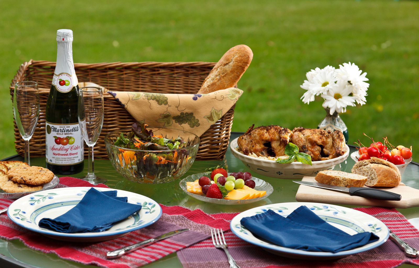 A picnic setup with food, drinks, and a bottle of sparkling cider.