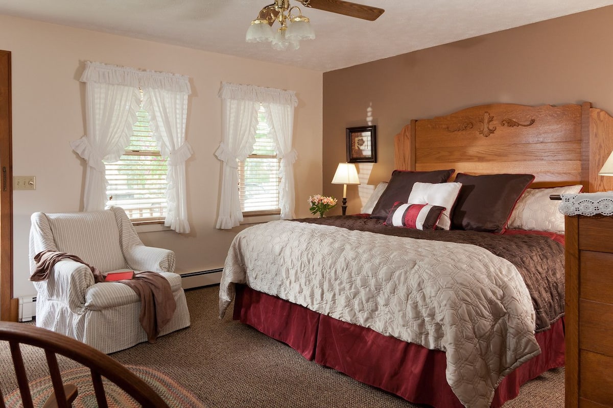 A bedroom with a bed, a chair, a wooden headboard, and a ceiling fan.