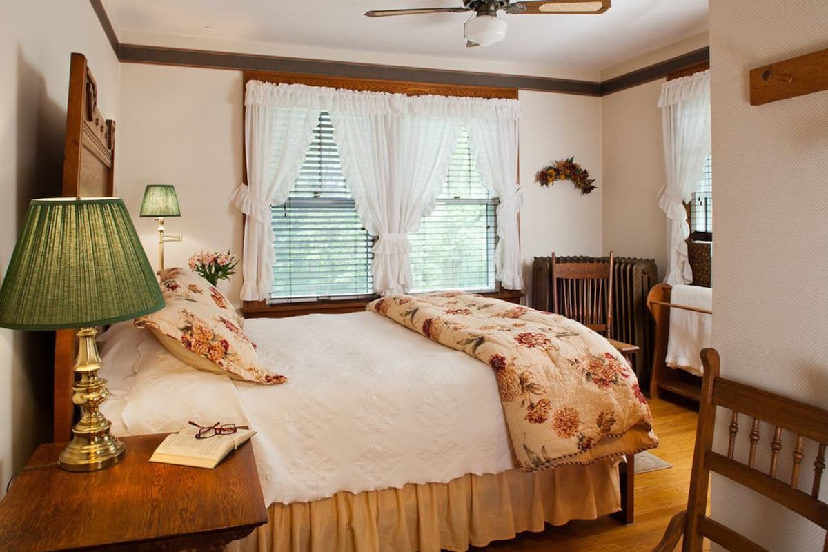 A bedroom with a bed, a nightstand with a lamp, a chair, and a window with curtains.