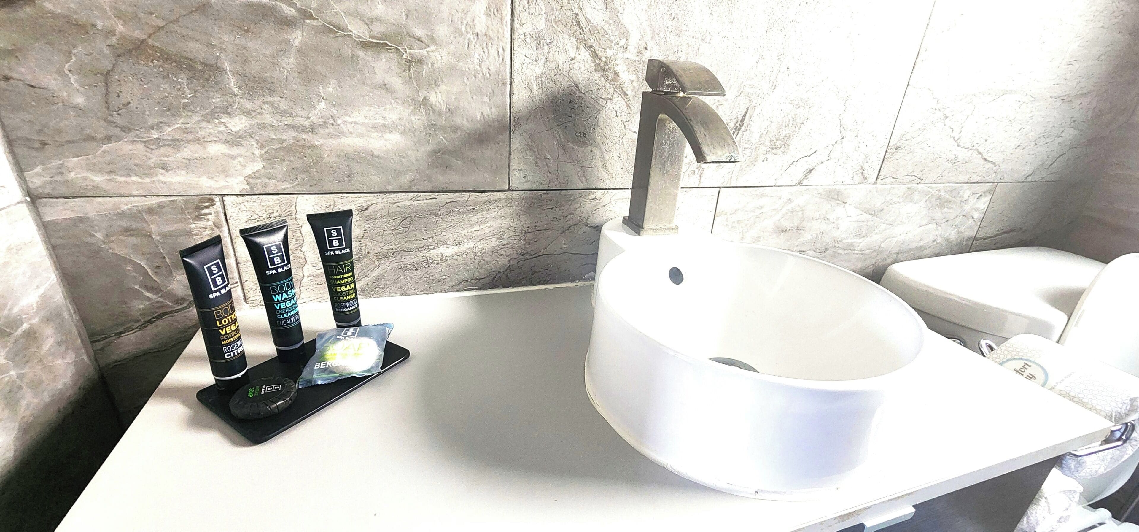 A bathroom with a white sink, a modern faucet, and three hair care products on the counter.