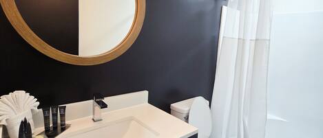 Une salle de bain moderne avec un grand miroir rond, un lavabo blanc, des toilettes et un espace douche.