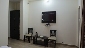 Een kamer met een aan de muur bevestigde televisie, twee stoelen, een kleine tafel met een koffiezetapparaat, en een deur.