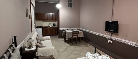 Habitación de hotel con cama, una mesita con toallas, kitchenette y televisor montado en la pared.