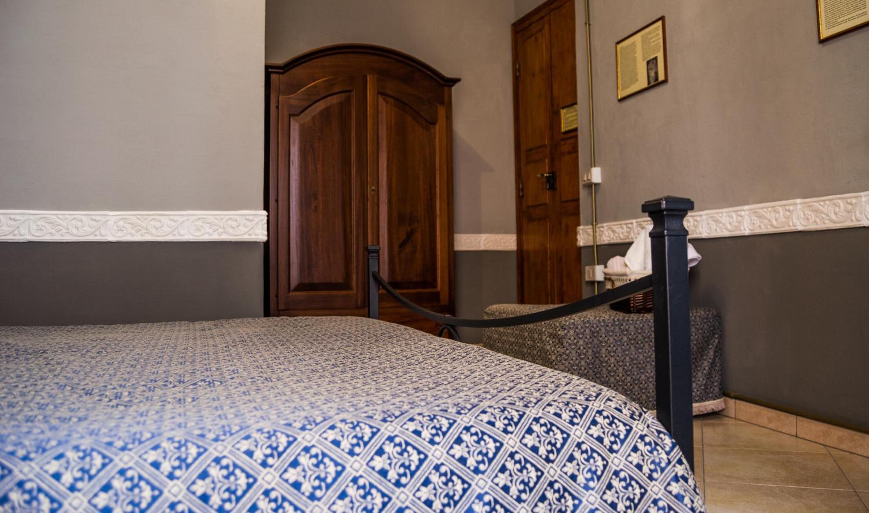 Quarto de hotel com colcha estampada, armário de madeira e um certificado emoldurado na parede.