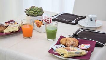 A breakfast table with a croissant, juice, a green smoothie, a muffin, and a cup of coffee.
