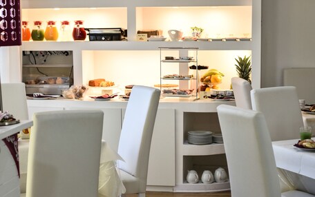 A breakfast buffet with various food items and beverages, white chairs, and a clean, modern interior.
