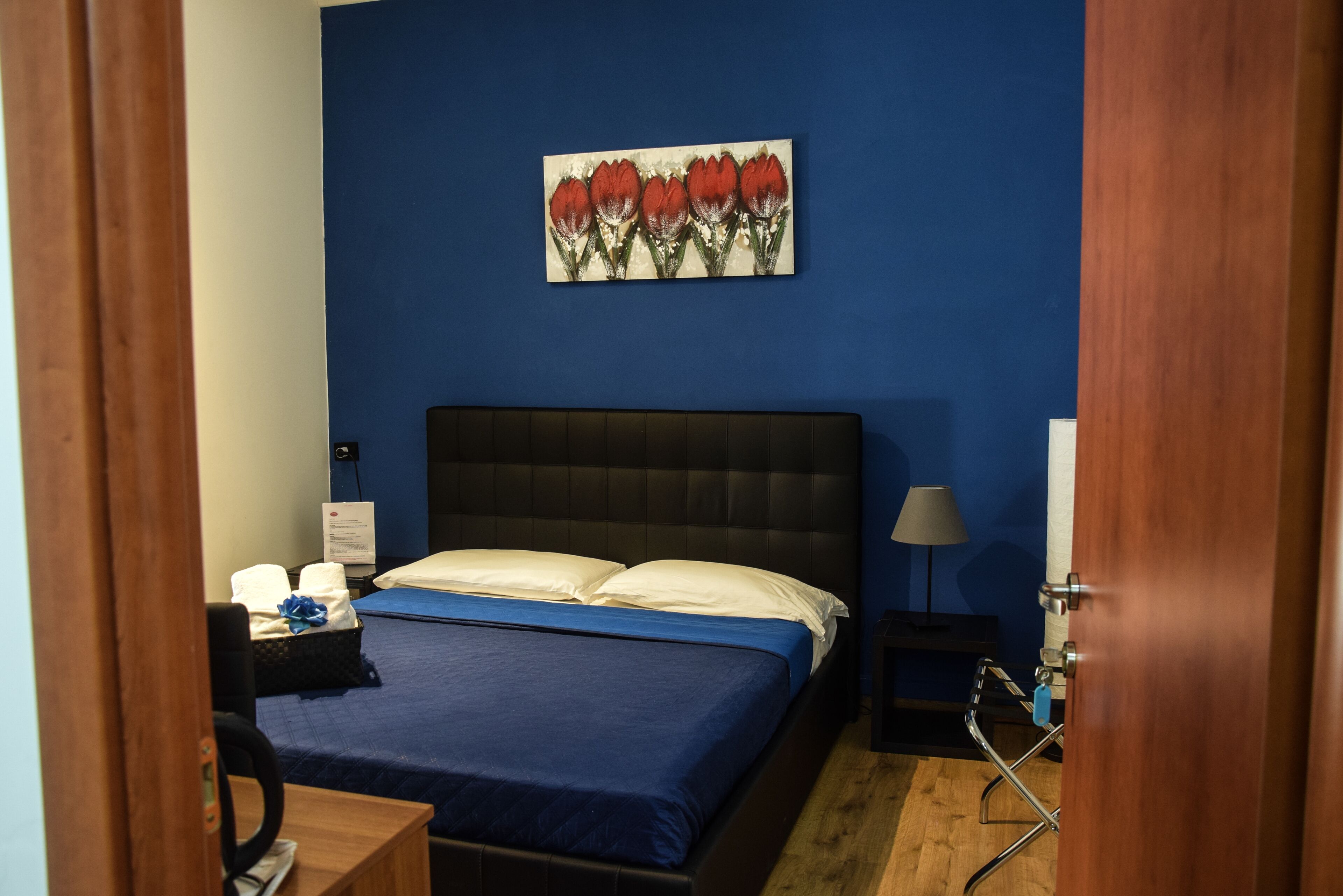 A hotel room with a bed, a nightstand, a lamp, and a painting on the wall.
