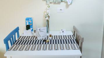 Un comedor con una mesa blanca y sillas azules, un adorno en la pared, un reloj y un jarrón con flores.