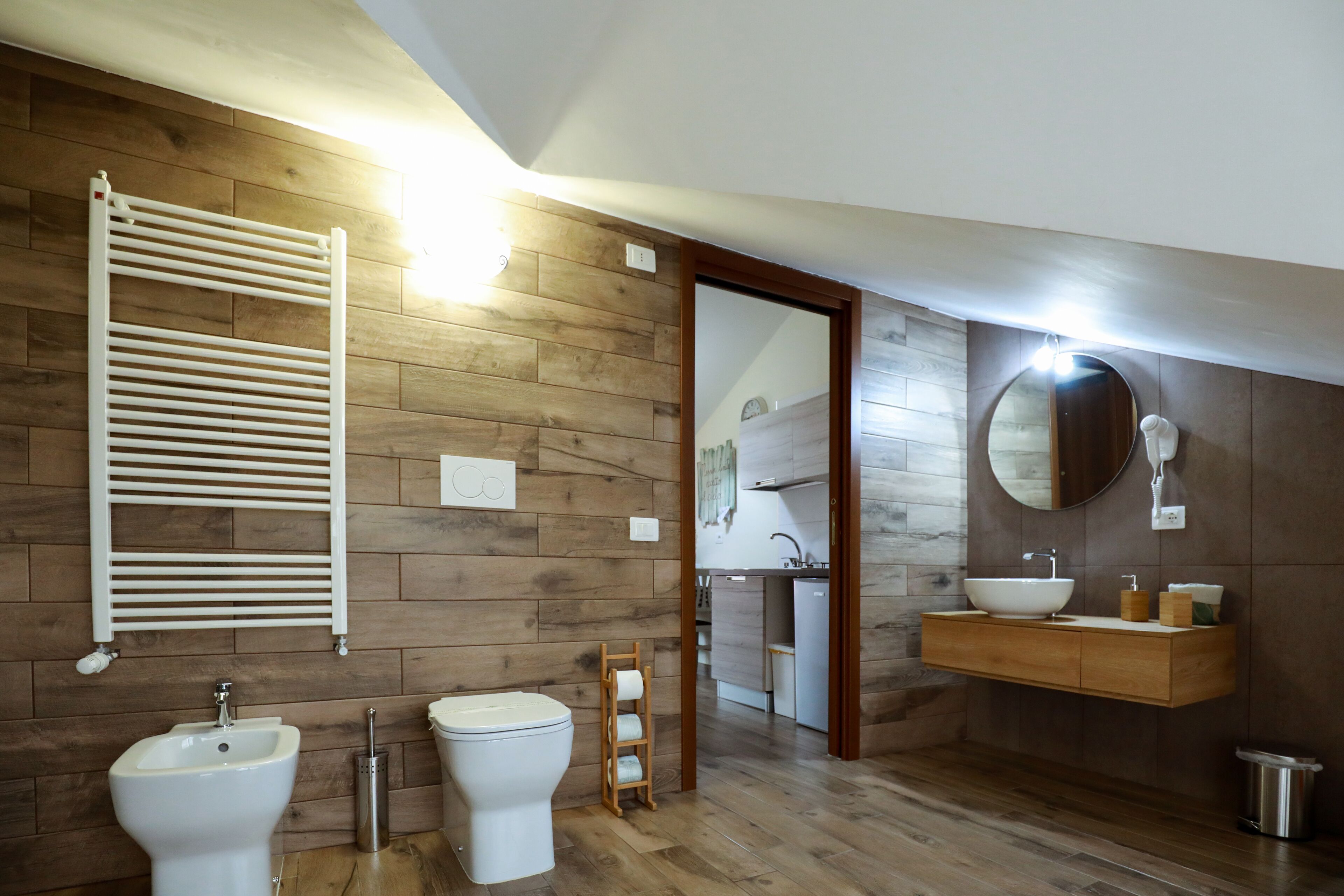Un baño moderno con pared de madera, un lavamanos blanco, un inodoro y un bidé.