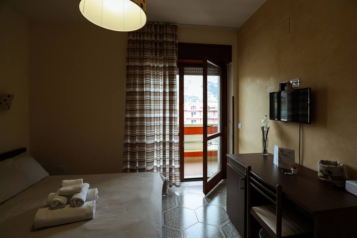 Habitación de hotel con cama, escritorio, televisor y vista al exterior.