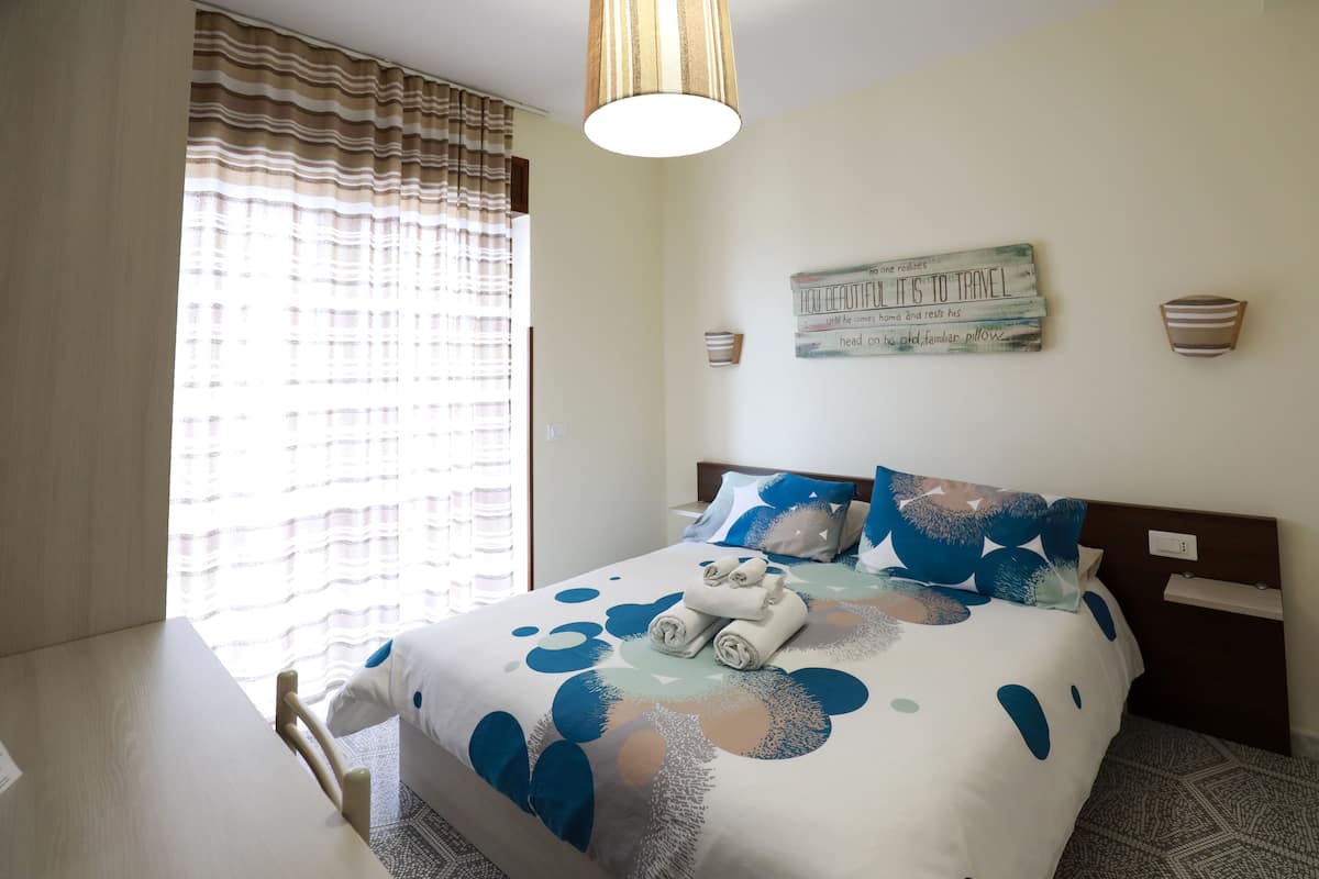 Habitación de hotel ordenada con cama, mesita de noche y ventana con cortinas.