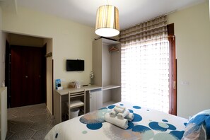 Hotelkamer met een bed, een bureau, een televisie, een kledingkast en een douche.