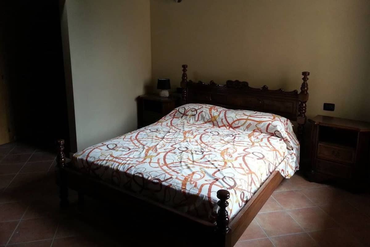 Un dormitorio con cama de madera, mesita de noche y lámpara fijada en la pared.