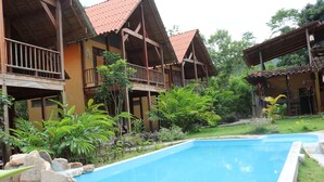 A pool area with a rectangular pool, wooden buildings with balconies, and surrounding greenery. - Canto del Rio Lodge (San Antonio de Cumbaza)