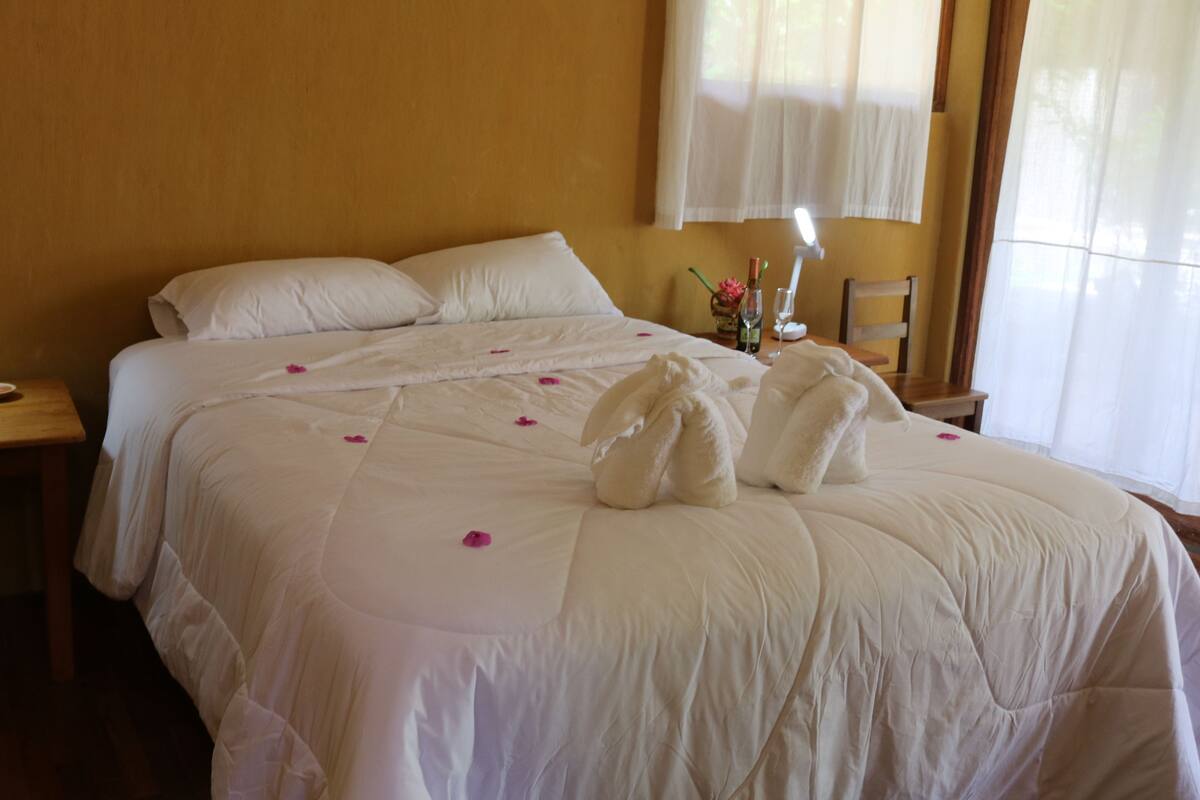 A hotel room with a large bed, a bedside table with a lamp, and a window with curtains.