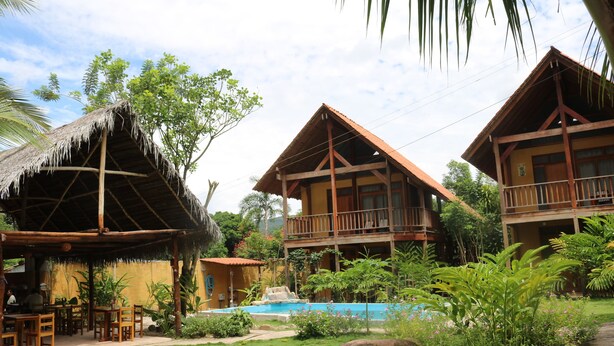 A resort with wooden cabins, a pool, and lush greenery. - Canto del Rio Lodge (San Antonio de Cumbaza)