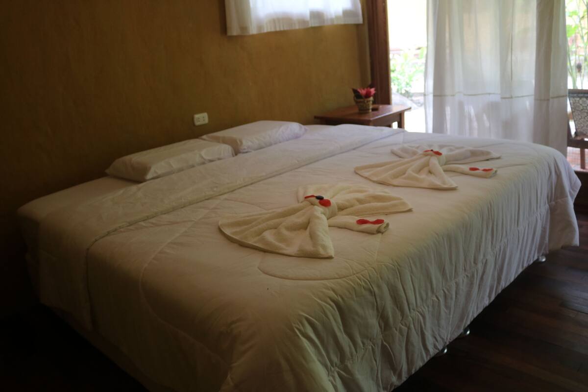 A hotel room with a large bed, a small table with a vase of flowers, and a window with curtains.