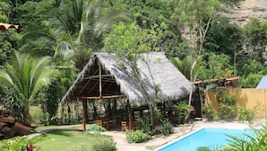 A thatched-roof hut with a pool and lush greenery. - Canto del Rio Lodge (San Antonio de Cumbaza)