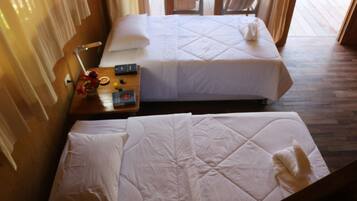 A hotel room with two beds, a wooden floor, a nightstand with a lamp, and a window with curtains.