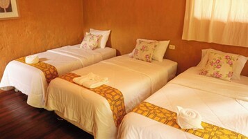 Una habitación con tres camas, cada una con una colcha blanca y un cubrecolchón estampado en amarillo.