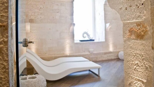 A room with a white, curved bench, a small window with a decorative element, and a stone wall with a textured surface.