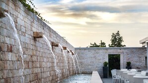 A stone wall with a water feature, outdoor seating, and a view of trees.