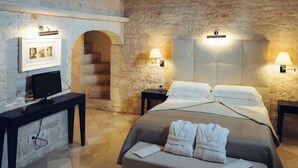 A bedroom with a stone wall, a bed, a desk, and a staircase.