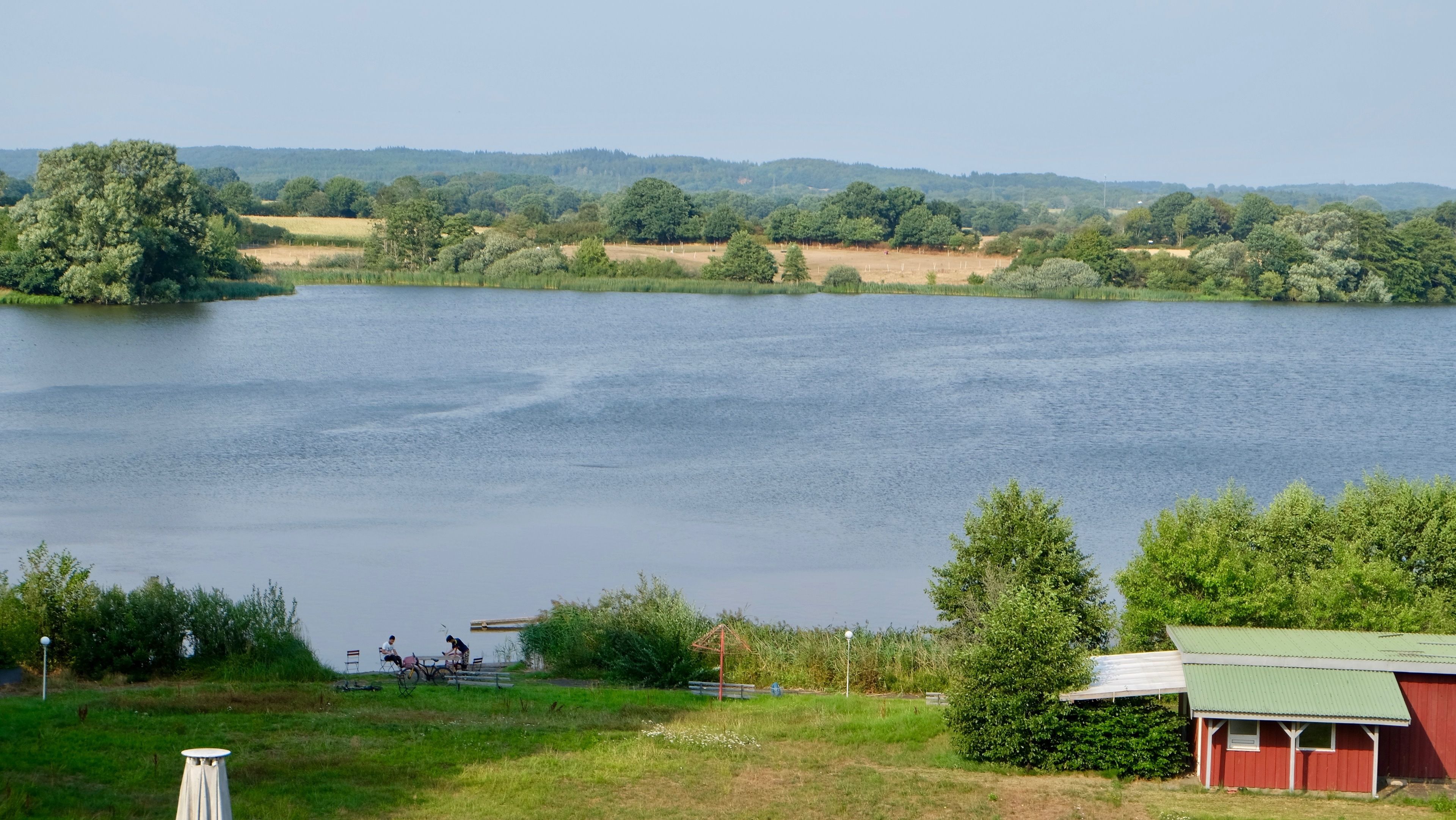 A lakeside view with a red building, a gazebo, and a person playing a guitar.