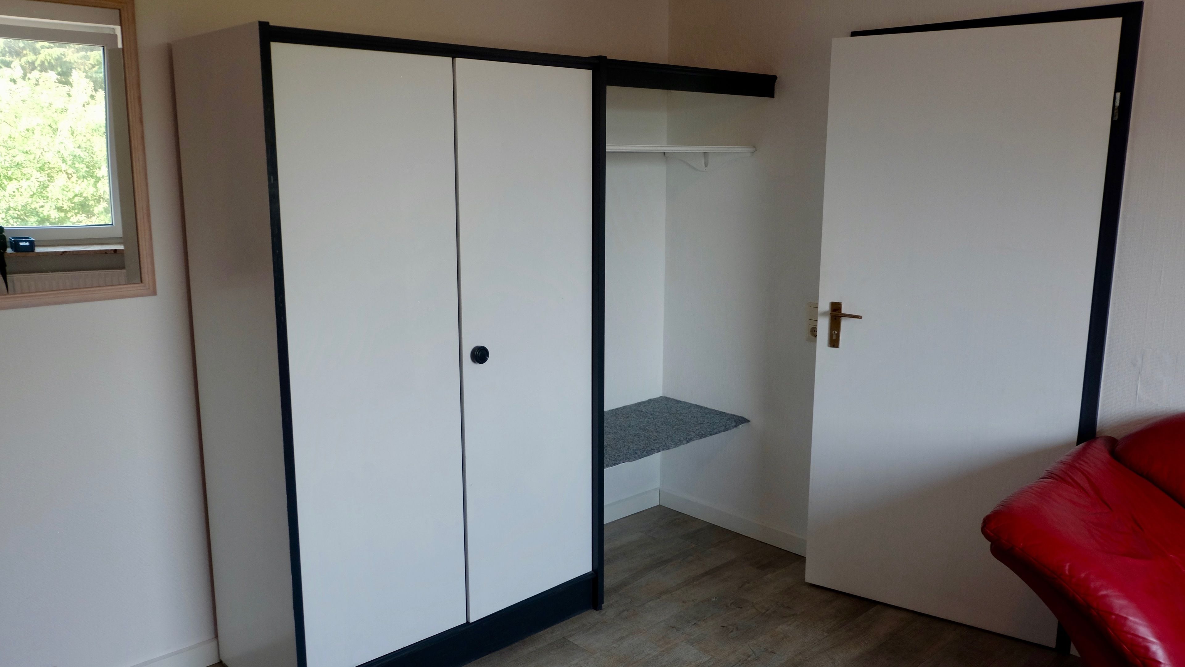 A room with a wardrobe, a small shelf, and a red chair.